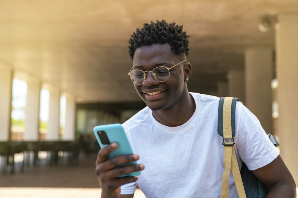 happy young student sitting and using his mobile phone in the university - Education concept